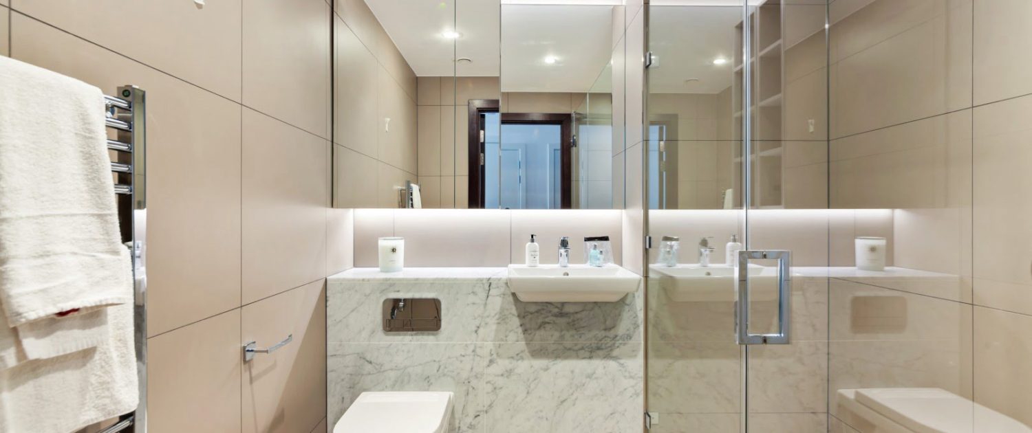 Modern bathroom interior showcasing a wall-mounted toilet, a bidet, marble countertops, a large mirror, glass shower stall, and neutral tones.