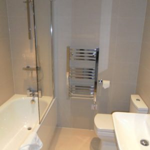 This image shows a modern bathroom with a bathtub, a glass shower screen, a heated towel rail, a toilet, and a basin, all in neutral tones.