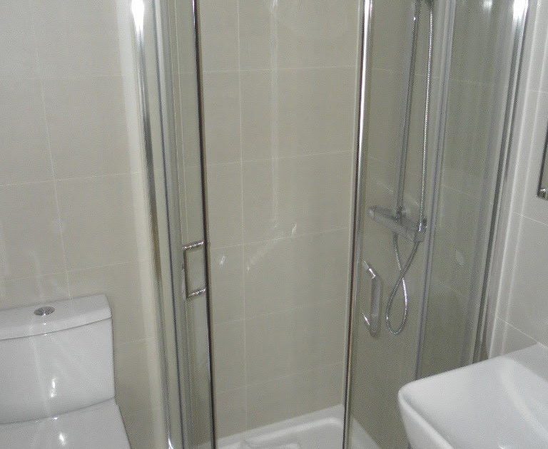 This image shows a modern bathroom with a curved glass shower enclosure, a silver shower head, a white toilet, and a sink with a mirror above.