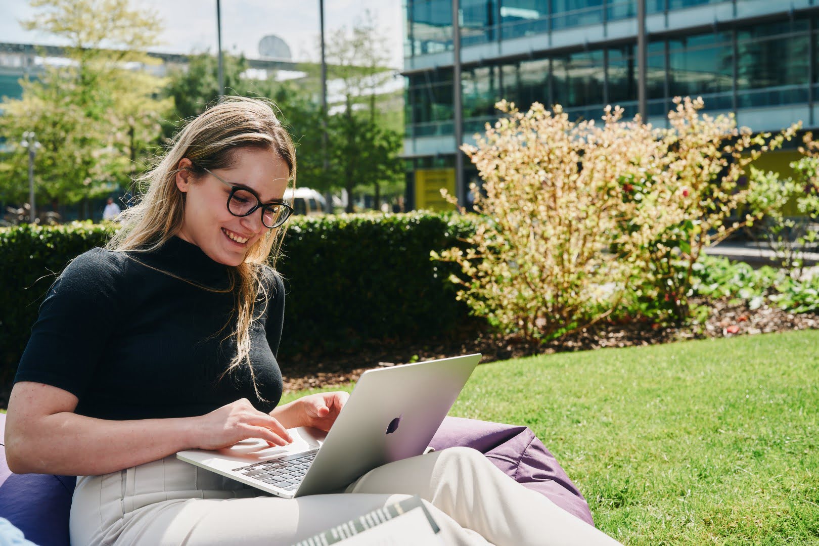 A person sits on the grass and uses a laptop.