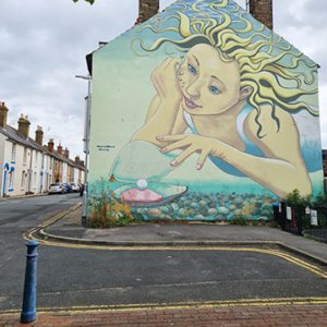 A cartoon mural of a sky filled with clouds is being painted and drawn onto the outdoor street art graffiti.