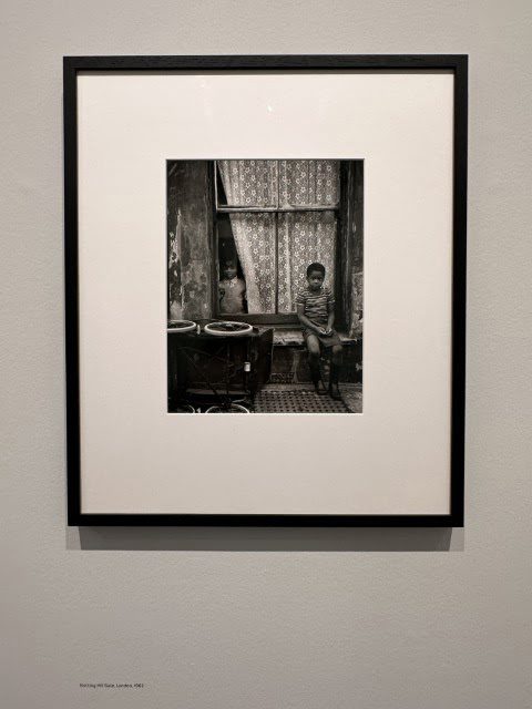 A black and white painting hangs in a picture frame in an art gallery, surrounded by photographic paper and other artwork on display in the art exhibition room.