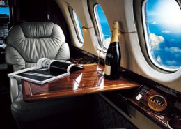 A luxury airline seat with a bottle of champagne and brand magazine open