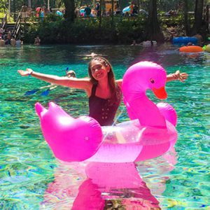 A person is smiling while floating in pink water on their outdoor vacation.